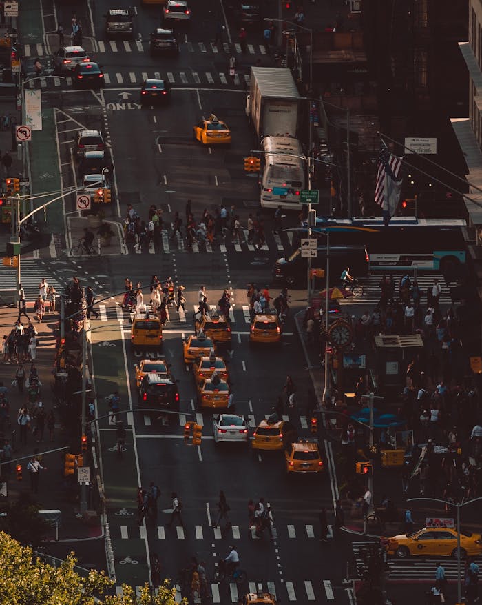 Aerial view of a busy intersection in Queens, NY, with cars, taxis, and pedestrians.
